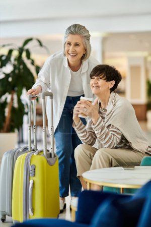 Senior lesbian couple embracing, carrying luggage in a hotel.
