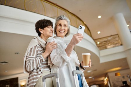 Foto de Una mujer sonriendo mientras se toma una selfie con su teléfono celular junto a su pareja. - Imagen libre de derechos