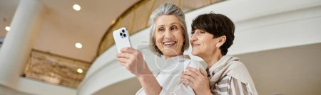 Senior lesbian couple joyfully taking a picture with her cell phone.