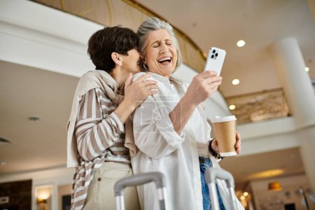 Téléchargez les photos : Senior lesbienne couple dans un hôtel capture un moment avec son téléphone. - en image libre de droit