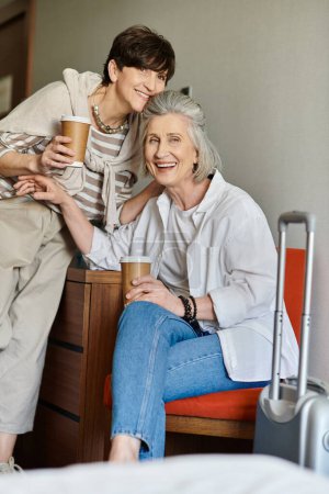 A senior lesbian couple, one holding a coffee cup, enjoying a moment together.