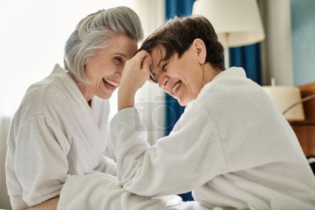 Deux femmes âgées partagent un moment de rire sur un lit confortable.