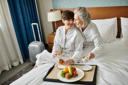 Senior lesbian couple sitting lovingly on a bed.