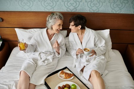 A senior lesbian couple sitting together in a cozy bed, sharing a moment of tranquility.