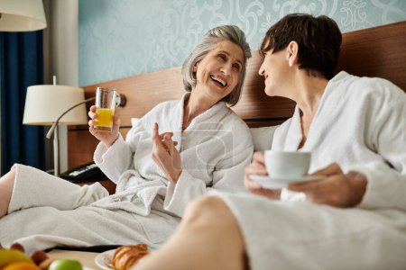 Dos mujeres mayores pacíficamente sentadas en una cama en un abrazo íntimo.