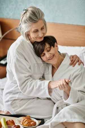 Tender moment between loving senior lesbian couple, hugging in bed.