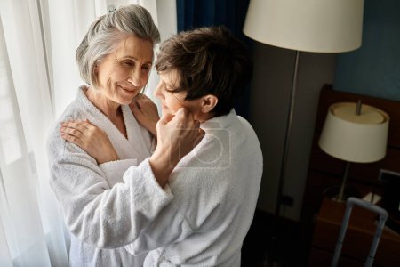 Photo for A senior lesbian couple in bathrobes sharing a tender embrace in a hotel. - Royalty Free Image