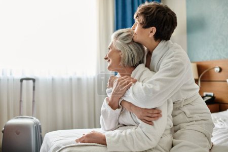 Ancianos lesbianas pareja compartir un tierno abrazo en un hotel habitación.