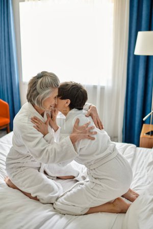 Two mature women relax on top of a bed in a comfortable setting.