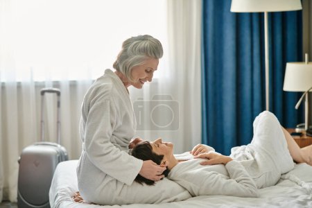Una pareja lesbiana mayor abrazándose tiernamente mientras está acostada en una cama.