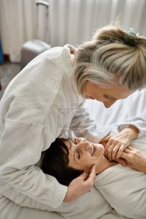 Tender senior lesbian couple in bed, one woman touches the others face lovingly.