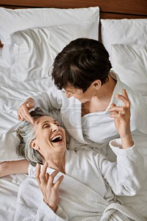 Photo for Senior lesbian couple embrace lovingly while laying in bed. - Royalty Free Image
