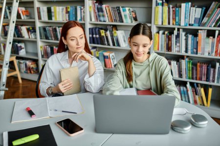 Photo for A tutor with red hair helps a teenage girl with after-school lessons on a laptop in a serene library setting. - Royalty Free Image