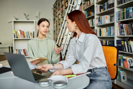 Un tuteur roux s'engage dans des leçons après l'école avec une adolescente à une table de bibliothèque, en utilisant un ordinateur portable pour l'éducation moderne.