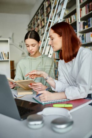 Ein Nachhilfelehrer mit roten Haaren führt einen Teenager in einer Bibliothek, beide zutiefst fokussiert auf ihren Laptop-Bildschirm für den After-School-Unterricht..