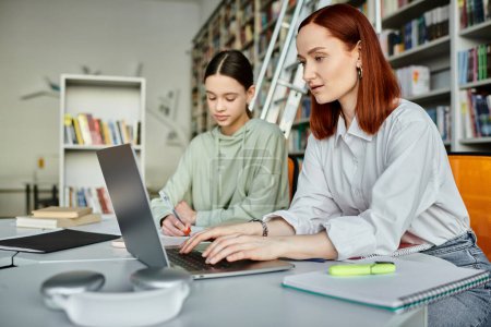 Tuteur rousse s'engage dans une leçon de tutorat après l'école avec une adolescente dans un cadre de bibliothèque, tous deux axés sur ordinateur portable.