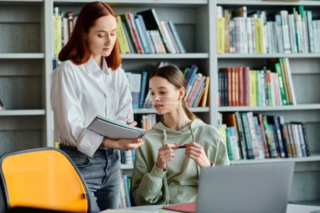 A redhead tutor is teaching a teenage girl in a library, with a laptop in front of them for their modern after-school lessons.