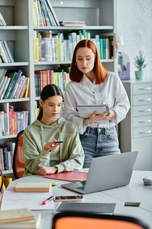 Rotschopf-Tutorin und Teenager-Mädchen in der Bibliothek, vertieft in Laptop-Unterricht für moderne Bildung.