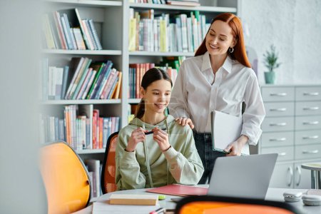 Photo for A redhead tutor teaches a teenage girl after school, sitting at a desk with a laptop in a modern office setting. - Royalty Free Image