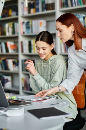 A tutor with red hair teaches a teenage girl in a library, as they work together on a laptop for their modern education.