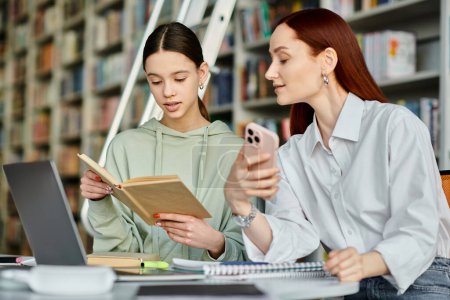 Téléchargez les photos : Un tuteur roux et une adolescente, absorbés dans un livre à une table de bibliothèque, apprenant ensemble. - en image libre de droit