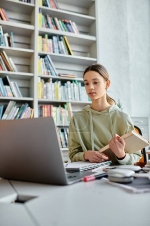 Un adolescent engagé dans l'éducation moderne, entouré de livres et d'un ordinateur portable, faisant ses devoirs avec diligence à un bureau.