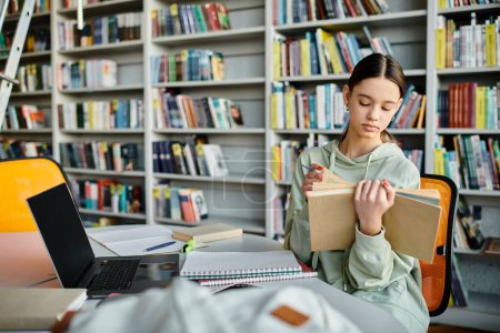Téléchargez les photos : Une adolescente engagée dans un livre à une table de bibliothèque, concentrée et immergée dans sa lecture. - en image libre de droit