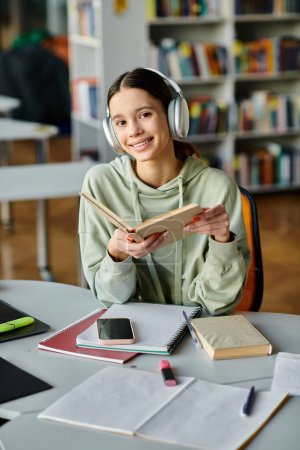 Una adolescente absorta en un libro con auriculares, inmersa en una tranquila soledad en una biblioteca.