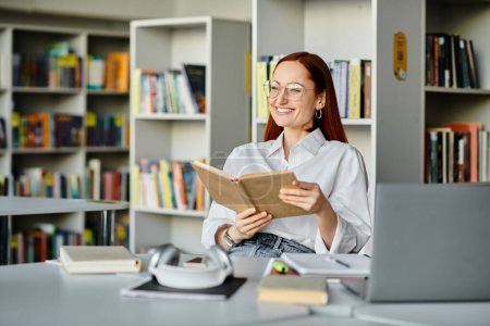 Una mujer pelirroja absorta en un libro, rodeada de estantes de libros en una biblioteca, absorbiendo el conocimiento.