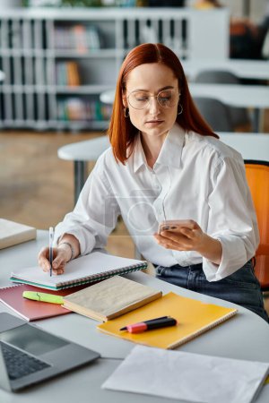 Photo for A redhead female tutor providing online teaching services, managing her laptop and cell phone after a school lesson. - Royalty Free Image