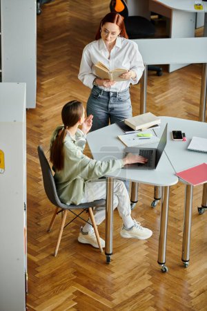 Téléchargez les photos : Une rousse encadre une adolescente dans un bureau moderne, travaillant ensemble sur un ordinateur portable pour des cours après l'école. - en image libre de droit
