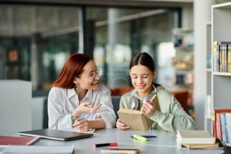 Una mujer pelirroja enseña a una adolescente en una biblioteca, absorta en lecciones extraescolares con una computadora portátil.