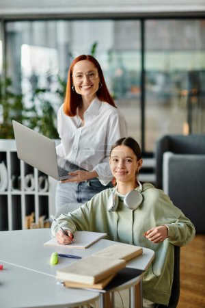 A redhead woman is teaching a teenage girl in an office setting, using a laptop for after-school lessons.