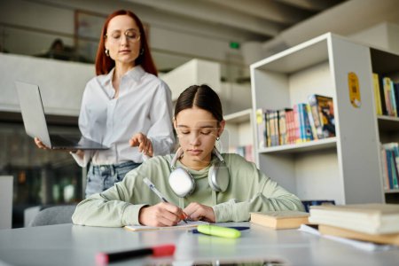Redhead woman tutors teenage girl at desk, both focused on laptop with headphones on.