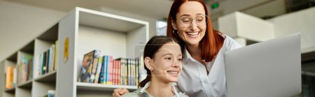 Photo for A redheaded woman holds a laptop in front of a bookshelf while teaching a teenage girl, redefining modern education. - Royalty Free Image
