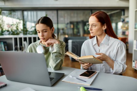 Eine rothaarige Frau unterrichtet ein Mädchen im Teenager-Alter, während sie an einem Tisch sitzen, beide fokussiert auf einen Laptop-Bildschirm während einer After-School-Stunde.