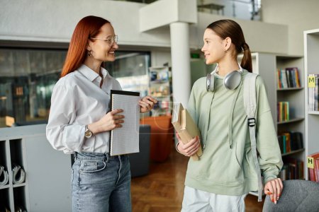 A redhead woman tutors a teenage girl in a library, engaging in after-school lessons