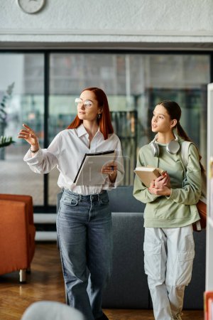 Photo for A redhead woman is teaching a teenage girl in an office setting, engaging in after-school lessons - Royalty Free Image