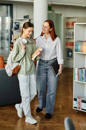Téléchargez les photos : Séance de tutorat entre une rousse et une adolescente dans une bibliothèque, engageant une conversation profonde - en image libre de droit