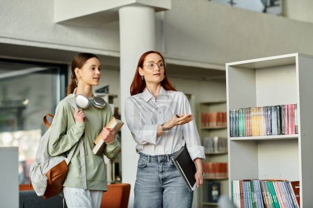 Eine rothaarige Frau unterrichtet ein Teenager-Mädchen in einer Bibliothek, vertieft in Bücher