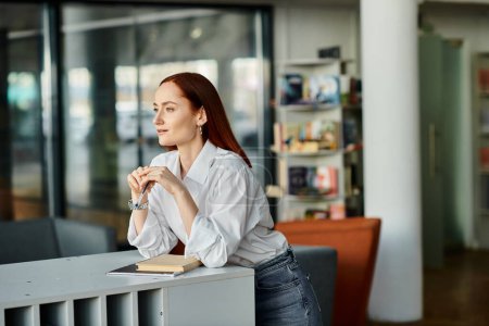 A redhead woman sitting at desk in a library, modern education.