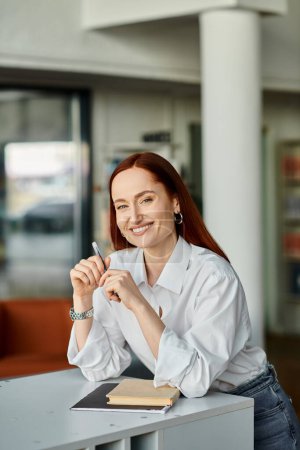 Téléchargez les photos : A redheaded woman sitting at a desk with a pen in hand, tutoring at after-school lessons. - en image libre de droit