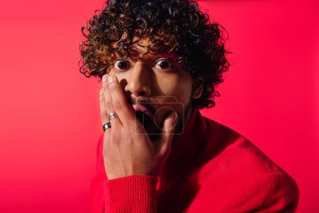 Handsome Indian man with curly hair strikes a pose in a bright red sweater.