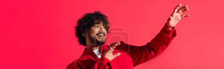 A handsome young Indian man in a vibrant red jacket strikes a dramatic gesture.