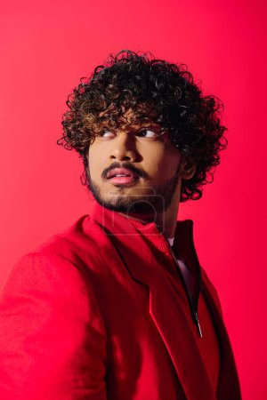Young Indian man with curly hair showcasing red jacket on vivid backdrop.