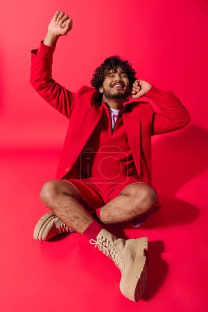 Téléchargez les photos : Un jeune homme élégant dans un costume rouge vibrant s'assoit soigneusement sur le sol. - en image libre de droit