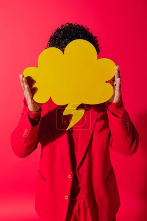 A handsome young Indian man in a vibrant outfit holding a speech bubble over his face.
