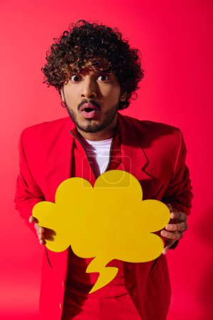 Stylish young man in red suit holding bright yellow speech bubble.