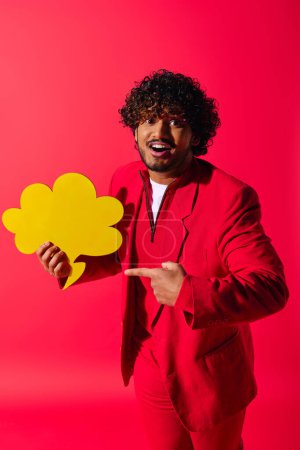 Guapo joven indio con un traje rojo sosteniendo una burbuja de habla amarilla sobre un fondo vívido.