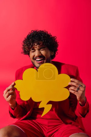 Handsome Indian man in red shirt poses with speech bubble on vibrant backdrop.